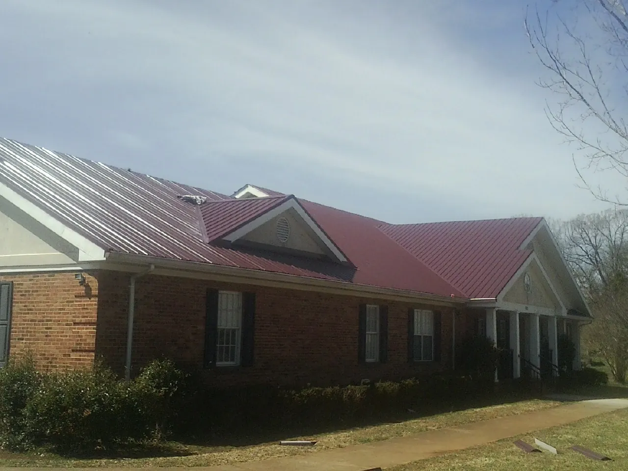 Red metal roof with gabled entries on a long brick building, from a Hail Damage Roof Repair job in Viola